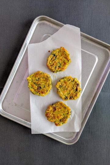 Four zucchini patties in a tray with parchment paper