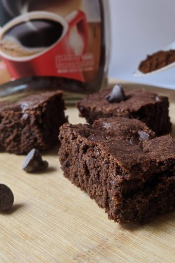 Espresso brownies sitting on a serving board, with espresso powder blurred in the background.