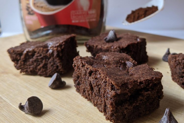 Espresso brownies sitting on a serving board, with espresso powder blurred in the background.