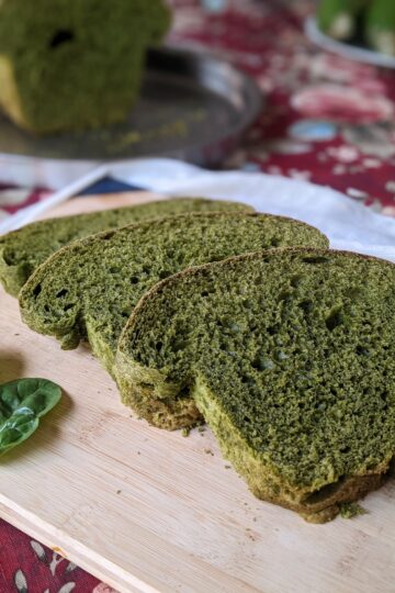 Spinach sandwich bread on cutting board, side view with loaf in background