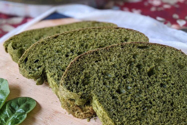 Spinach sandwich bread on cutting board, side view with loaf in background