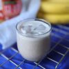 Peanut butter smoothie in glass with jar, cloth, and bananas in background