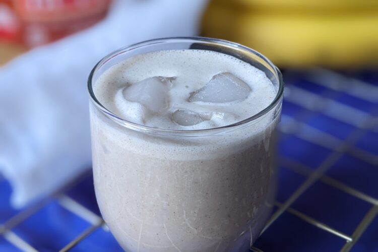 Peanut butter smoothie in glass with jar, cloth, and bananas in background