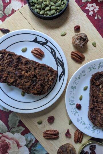 Dried Fruit & Nut Loaf in plates on cutting board with pecans, figs, and cranberries